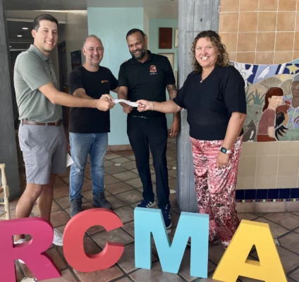 Four people smiling and holding a hole-in-one winner's check behind large, colorful block letters spelling "RCMA".