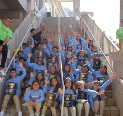Immokalee Community Academy National Beta Club students and staff celebrating on outdoor stairs while holding awards and plaques.